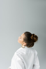 young model in white shirt and hoop earring posing isolated on grey with copy space.