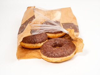 Chocolate donut with chocolate chips in a paper bag on a white background. close-up.