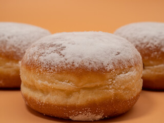 Freshly baked and dusted with powdered sugar German donuts. Donut berliner or krapfen on orange background.