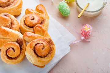 Easter breakfast Holliday concept. Easter bunny buns rolls with cinnamon made from yeast dough with orange glaze, easter decorations, colored eggs on pink spring background. Easter Holliday card.