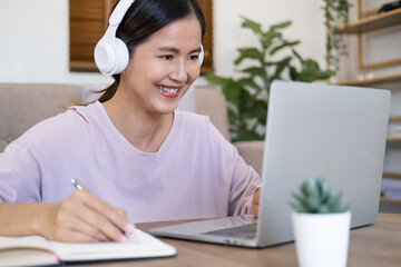 Happy young woman learn language listen lecture watch webinar write notes look at laptop sit in...