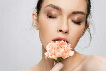 Obraz na płótnie Canvas young woman with makeup and closed eyes holding peach carnation near face isolated on grey.
