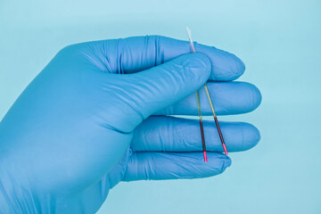 hand in medical glove holding microhematocrit tube on blue background.