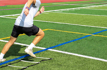 High school football player running though the ladder on a turf field