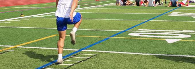 Football player running through a ladder on a turf field