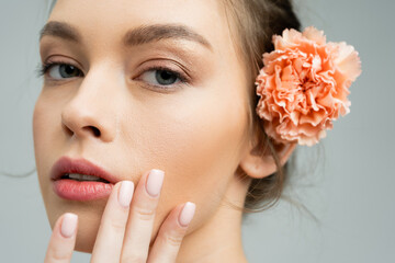 close up portrait of sensual woman with natural makeup and peach carnation behind ear touching face...