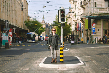 Fototapeta premium Outdoor portrait of handsome young man posing in the middle of the road next to traffic light