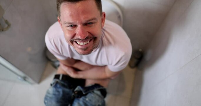 A smiling man sits on the toilet, front view