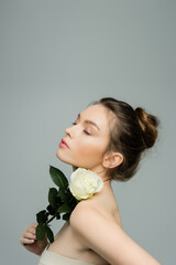 sensual woman with closed eyes holding fresh rose near naked shoulder isolated on grey.