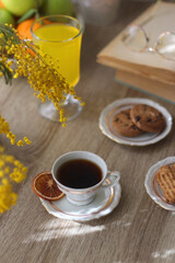 Cup of tea, plates with cookies, glass of orange juice, books, reading glasses, bowl of fruit and candles on the table. Selective focus.