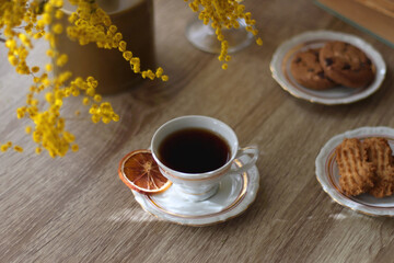 Cup of tea, plates with cookies, glass of orange juice, books, reading glasses, bowl of fruit and candles on the table. Selective focus.