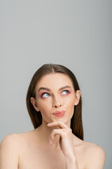 Dreamy woman with bright visage and naked shoulders looking up isolated on grey.