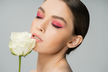 Naklejka premium portrait of pretty woman with pink eye shadows near fresh rose isolated on grey.