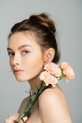 Young fair haired woman with naked shoulders holding carnations isolated on grey.