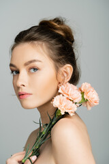 Fototapeta premium Young fair haired woman with naked shoulders holding carnations isolated on grey.