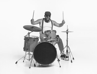 Portrait of emotive, expressive man in sunglasses playing drums, performing isolated over white...