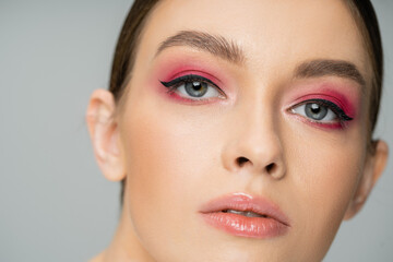 close up portrait of young woman with pink makeup looking at camera isolated on grey.