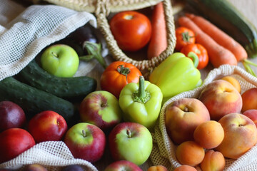 Straw bag and reusable fabric bags filled with various healthy fruit and vegetables. Wooden background, selective focus.