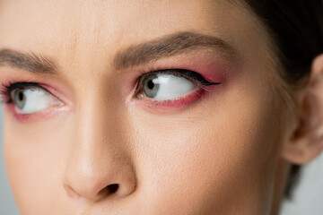Cropped view of young woman with pink eye shadow looking away isolated on grey.