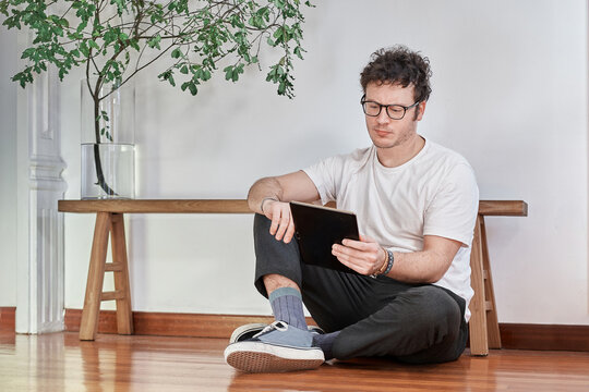 Portrait of a young white man sitting on floor and working with a tablet