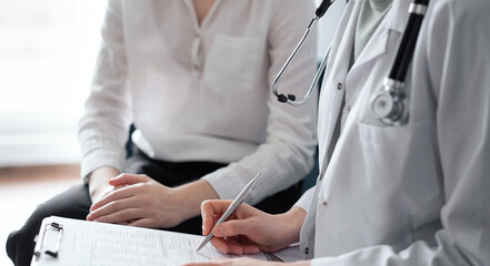 Doctor and patient sitting at sofa in clinic office. The focus is on female physician's hands filling up the medication history record form, close up. Medicine concept