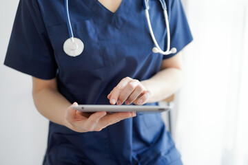 Doctor woman using tablet computer while standing near panorama window in clinic, close up. Physician or surgeon at work. Medicine concept