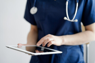 Doctor woman using tablet computer while standing near panorama window in clinic, close up....