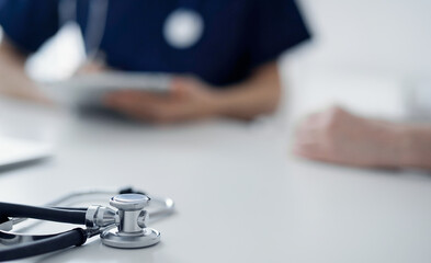 Stethoscope lying on the tablet computer in front of a doctor and patient at the background. Medicine, healthcare concept