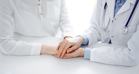 Doctor and patient sitting near each other at the table in clinic office. The focus is on female physician's hands reassuring woman, only hands, close up. Medicine concept