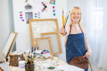 Young artist is holding her paintbrushes in her hand, and she is holding them in front of her