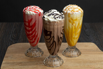 Fresh tasty milkshakes of strawberry, chocolate, and Vanilla on a wooden tray 