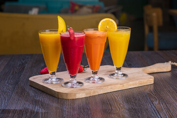 Fresh pressed juices of Mango, strawberry, orange and carrots on a wooden tray 