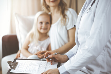 Doctor and patient. Pediatrician using clipboard while examining little girl with her mother at home. Happy cute caucasian child at medical exam. Medicine concept