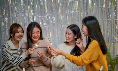 Cheerful friends enjoying home Birthday holiday party. Asian Friends hold lights with sparkling Sparkler celebrating Christmas or New Year eve party.