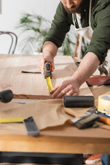 Cropped view of bearded restorer measuring wooden board with ruler in workshop.