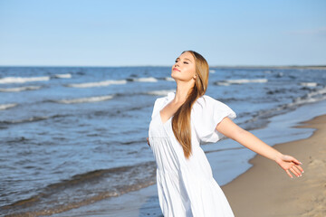 Happy, beautiful woman on the ocean beach standing in a white summer dress, open arms