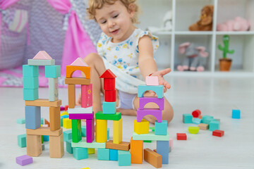 The child plays in the children's room with a wooden constructor. Selective focus.