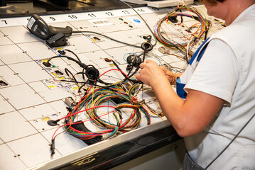 Hands of employees who check the quality of the wiring for cars at a modern plant on a special stand at the production shop