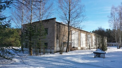 Fototapeta na wymiar Abandoned building for the storage of military equipment of the former Soviet military base in winter. An old hangar for automotive vehicles under a layer of snow in the middle of a pine forest.