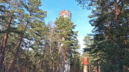 An old rusty water tower and a fire tower under a layer of snow in the middle of a dense spruce forest in winter. Frozen water turned into ice. Chernobyl in winter.