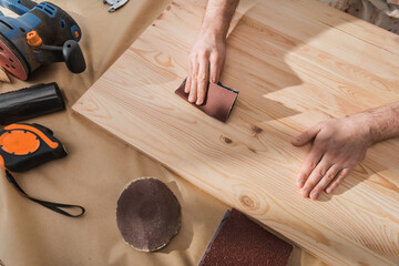 Top view of carpenter sanding wooden board near tools on table. - obrazy, fototapety, plakaty