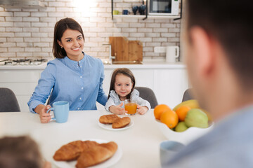 Mother with her little daughter having breakfast on modern kitchen. Family enjoying a healthy breakfast together