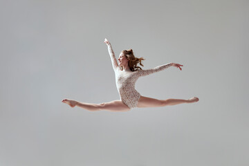 One beautiful young dancer in studio on grey background.  Flying  split.  Sport, ballet concept.