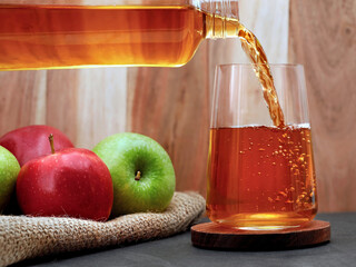 Fresh apple juice pours from a bottle into a glass on the table, Refreshing fruity juice made from delicious green and red apples