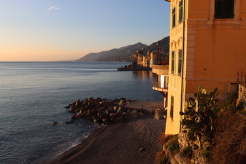 Fototapeta premium Camogli, Italy - January 27, 2023: Beautiful old mediterranean town at the sunrise time with illumination during winter days. People enjoying the evening at the beach with beautiful sunset background
