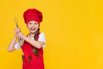 Fototapeta na wymiar Chef little girl holds a blender for whipping. A child in a red cap and apron on a yellow isolated background. A place for advertising. Copy space.