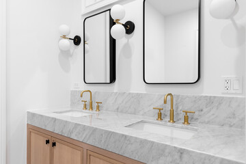 A bathroom with a white oak cabinet, marble countertop, gold faucets, black and white tiled floor,...