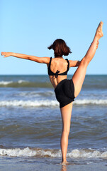 Fototapeta na wymiar girl does gymnastic exercises on sandy beach by the sea