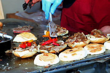 cook in the street food stall preparing a stuffed sandwich with meat and vegetables