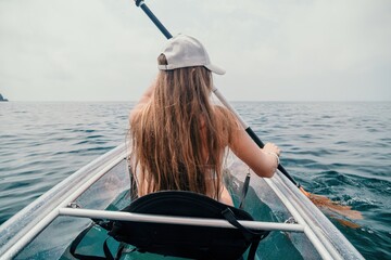 Woman in kayak back view. Happy young woman with long hair floating in transparent kayak on the crystal clear sea. Summer holiday vacation and cheerful female people relaxing having fun on the boat